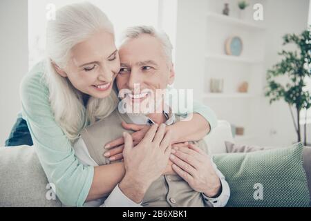 Gros plan photo d'une charmante femme dans un pull taal qui câlin son homme en regardant s'asseoir dans une salle lumineuse Banque D'Images