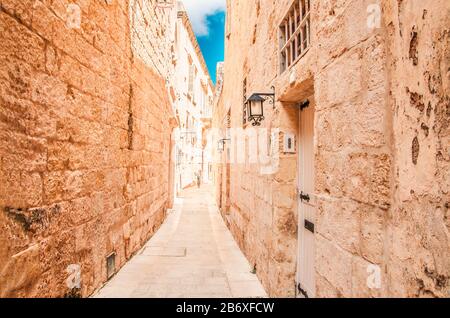 Mdina, Malte; 12 avril 2019: Rue de la vieille ville de Mdina avec lanternes rétro, murs en pierre de bâtiments de style arabe et une femme passe-by Banque D'Images