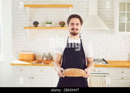 L'homme barbu de Baker tient dans ses mains du pain frais debout dans la cuisine. Banque D'Images