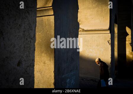 Un homme âgé dans des vêtements traditionnels traverse une arche ensoleillée au coucher du soleil à Fes, au Maroc Banque D'Images