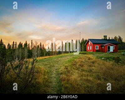 Petite maison rouge au milieu de la forêt, une chaude journée d'automne. La lumière du soleil fait briller les nuages. Banque D'Images