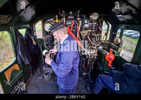 L'équipage du repose-pied verse une bière dans un pot d'étain à bord de la locomotive à vapeur Foremarke Hall Great Western Railway Modifield Hall Classe 7903, construite en 1949, qui transporte des passagers de la gare de Toddington aux courses de Cheltenham pendant le festival. Banque D'Images