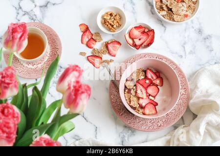 Scène de petit-déjeuner avec yaourt, céréales et bol à fraises séchées et une tasse de thé sur une table à plateau Banque D'Images