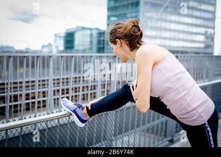 Junge Sportlerin macht Dehnübungen nach dem Sport in der Stadt. Le jeune sportif s'étire après les sports dans la ville. Banque D'Images