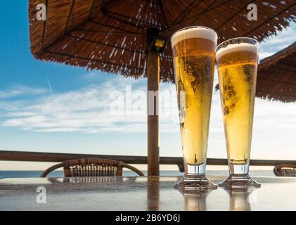 Deux verres de bière sur une table servis dans un restaurant de plage, avec mer méditerranéenne derrière. Banque D'Images