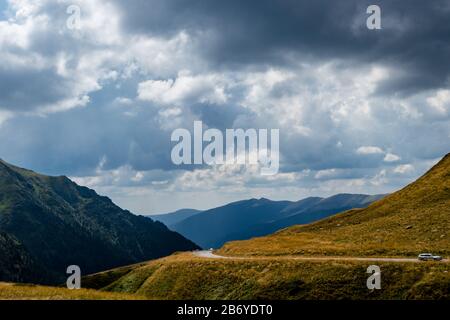 Voiture passant sur la route de montagne avec des montagnes en arrière-plan et des nuages sombres au-dessus Banque D'Images