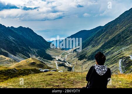 Femme regardant les voitures sur une route de montagne sinueuse passant par une vallée de montagne Banque D'Images