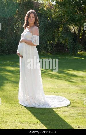 Belle jeune femme enceinte portant une longue robe blanche, cachant son bébé bosse Banque D'Images