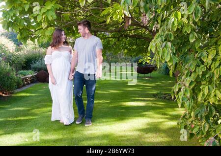 Belle jeune femme enceinte marchant main dans la main avec son partenaire un beau jour d'été Banque D'Images