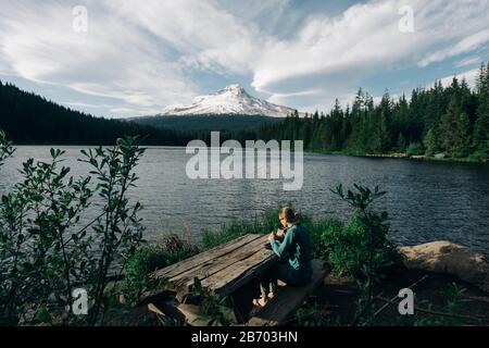 Une jeune femme mange un déjeuner à une table de pique-nique près d'un lac près du mont Capot. Banque D'Images