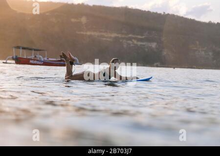 Femme surfant dans l'océan au coucher du soleil Banque D'Images