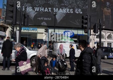 Les Londoniens et les visiteurs de Londres traversent Piccadilly Circus où la publicité numérique est affichée sur les grands écrans au-dessus d'une succursale de Barclays Bank et Boots the Chemist, le 6 mars 2020, à Londres, en Angleterre. Banque D'Images