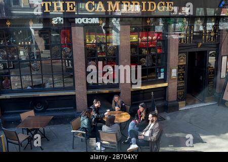Un groupe d'amis aiment prendre un verre à l'extérieur de Cambridge, un pub typique de Cambridge Circus dans le West End de Londres, le 12 mars 2020, à Londres, en Angleterre. Le Cambridge a été construit en 1887 sur le site Des armoiries du roi, à côté du Palace Theatre. Banque D'Images
