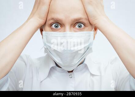 Portrait rapproché d'une jeune femme choquée portant un masque chirurgical protecteur tenant les mains sur la tête - concept d'épidémie de virus Banque D'Images