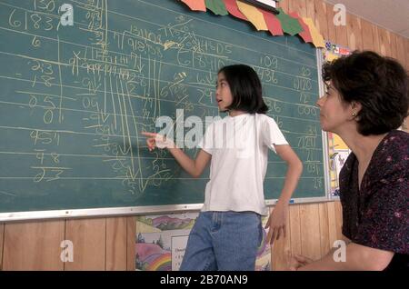 Austin Texas USA: Confiante vietnamienne-américaine de quatrième classe fille explique son travail sur un long problème de division au tableau noir comme le regarde l'enseignant. M. ©Bob Daemmrich Banque D'Images