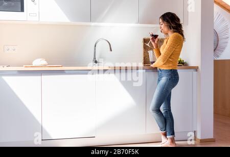 Femme buvant un verre de vin dans une cuisine moderne Banque D'Images