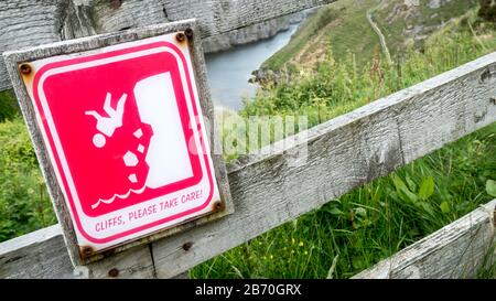 Panneau d'avertissement de sécurité sur les falaises de Smoo Cave, Écosse. Un signe illustré d'un visage de falaise. La chute est visible à travers la clôture. Banque D'Images