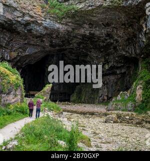 Grotte de Smoo, Durness, Écosse. Un couple touristique ajoute de l'échelle à la scène lorsqu'ils photographient l'entrée de la grotte de Smoo dans le nord de l'Écosse. Banque D'Images