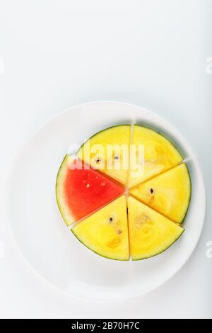 Morceaux de pastèque rouge et jaune dans une plaque ronde blanche, sur fond blanc. Vue de dessus. Une tranche de pastèque rouge est l'une des jaunes Banque D'Images
