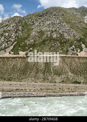 Vue sur la rivière Baspa en direction de l'Himalaya et des pentes rocheuses accidentées sous le ciel bleu en été près de Chitkul, Himachal Pradesh, Inde. Banque D'Images