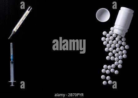Thermomètre médical, seringue jetable avec aiguille, flacon en plastique blanc, comprimés blancs dispersés sur la surface noire. Vue de dessus. Le sujet de m Banque D'Images