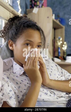 Une jeune fille afro-américaine de 14 ans souffle son nez alors qu'elle est malade à la maison au lit. ©Bob Daemmrich Banque D'Images