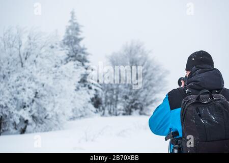Vue arrière d'un photographe de voyage photographiant une forêt enneigée debout dans une neige et dans le brouillard lors d'une journée hivernale glaciale. Concept de voyage d'un natu Banque D'Images