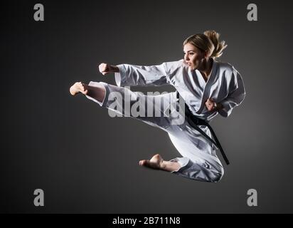 Image composite d'une fille de karaté dans un kimono blanc avec ceinture noire en saut. Fond violet et nuages de fumée Banque D'Images