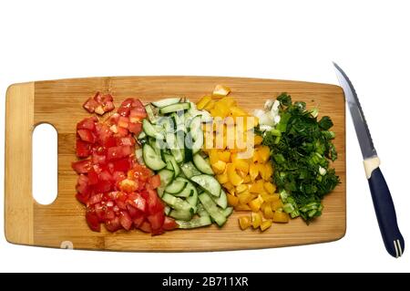 Vue de dessus du processus de cuisson de la salade végétarienne. Tomates, concombre, paprika et légumes verts tranchés sur planche à découper en bois Banque D'Images