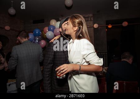 Beau homme avec une jeune femme baisonne de barbe dans une joue, la féliciter avec son anniversaire. Ballons colorés sur l'arrière-plan. Fille tenant une savoureuse Banque D'Images