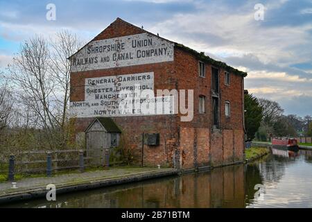 Vieux bâtiment de quai de canal délabré à Ellesmere Shropshire à côté du canal, sur un hiver froid et calme avec un narrowboat en arrière-plan. Banque D'Images