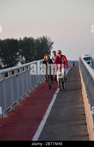 De l'autre côté du pont, il y a trois cyclistes à vélo le long de la piste cyclable Banque D'Images