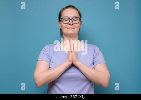 Femme caucasienne mûre dans des verres tenant les mains avec les yeux fermés. Méditez ou faites un souhait, en essayant de calmer. Banque D'Images