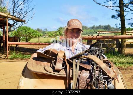 Une jeune cowgirl souriante et attrayante portant une grande selle de cheval en cuir à 900 acres Gunstock Ranch, Oahu Island, Laie, Hawaï, États-Unis Banque D'Images