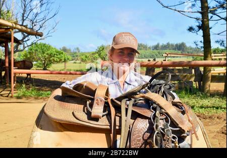 Une jeune cowgirl souriante et attrayante portant une grande selle de cheval en cuir à 900 acres Gunstock Ranch, Oahu Island, Laie, Hawaï, États-Unis Banque D'Images