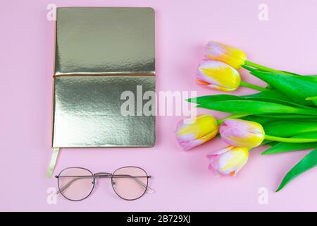 pinc coloré et tulipe jaune avec carnet et lunettes plat posé isolé sur pinc vue de dessus d'arrière-plan. Fleur de printemps. Fête des femmes, fête des mères Banque D'Images