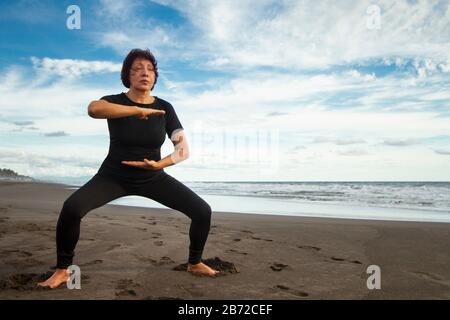 Femme active senior pratiquant le Tai chi sur la plage. Banque D'Images