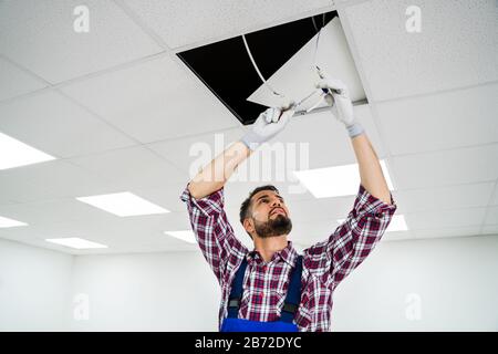 Portrait de l'électricien sur l'escabeau installe l'éclairage pour le plafond In Office Banque D'Images