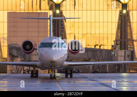 Un petit avion se tient sur la plate-forme du tablier à l'arrière-plan d'un terminal en verre avec lumière de coucher réfléchie dans le ciel Banque D'Images