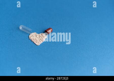 Granules versés à partir d'une capsule en forme de coeur sur un fond bleu classique. Médicaments en forme de coeur. Symbole de coeur dessiné par des pilules. Banque D'Images