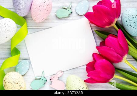 Carte de vœux. Fleurs de tulipes printanières, œufs de pâques et décorations sur fond en bois blanc d'en haut dans un style plat. Banque D'Images