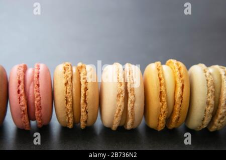 Rangée de macarons colorés français sur fond noir foncé avec espace de copie pour le texte. Banque D'Images