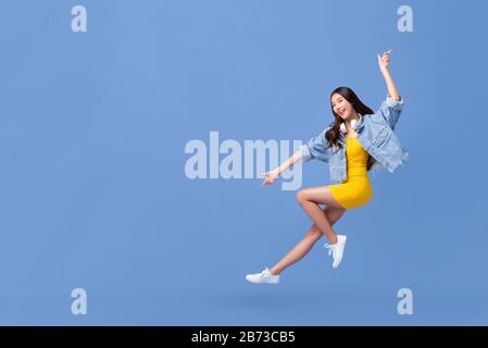 Jeune fille asiatique souriante en plein air avec la main pointant vers le haut et vers le bas isolée sur fond bleu clair avec espace de copie Banque D'Images