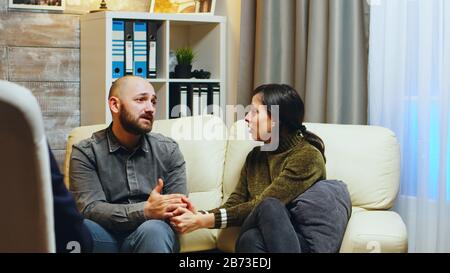 Une petite amie triste tenant les mains du mari assis sur le canapé lors d'une thérapie de couple. Thérapeute donnant des conseils au couple stressé. Banque D'Images