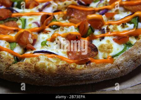 Pizza avec tranches de pepperoni et de poivre, surmontée de fromage et sauce orange chaude sur fond de carton artisanal, vue latérale. Stocker la photo pour le Web et l'impression. Banque D'Images