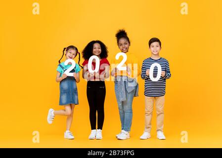 Mignons enfants de course mixtes souriant et portant les numéros 2020 pour le concept de nouvelle année isolé sur fond jaune Banque D'Images