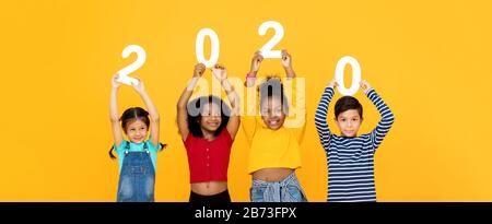 Mignons enfants de course mixtes souriant et portant les numéros 2020 pour le concept de nouvelle année isolé sur fond de bannière jaune Banque D'Images