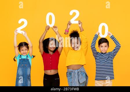 Mignons enfants de course mixtes souriant et portant les numéros 2020 pour le concept de nouvelle année isolé sur fond jaune Banque D'Images