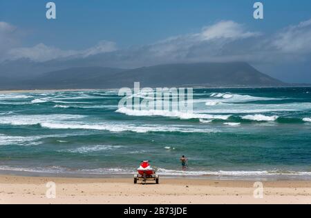 Kleinmond, Cap-Occidental, Afrique Du Sud. Déc 2019. Scooter d'eau sur la plage et pêche de garçon avec toile de fond de vagues blanches et de montagnes. Banque D'Images