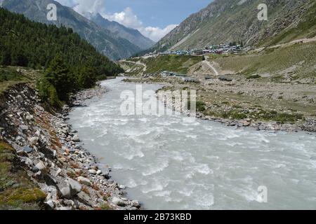 Vue sur la rivière Baspa vers les Himalaya accidentés et le petit village de Chitku sous le ciel bleu dans l'Himachal Pradesh, Inde. Banque D'Images